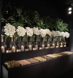 several vases filled with flowers and candles on a wall behind a buffet table full of food