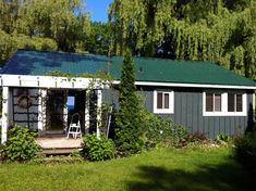 a small house with a green roof and white shutters on the front door is surrounded by greenery