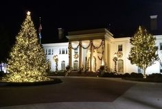 a large white house with christmas lights on it's trees and bushes in front