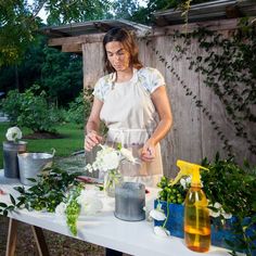 a woman in an apron is arranging flowers on a table with bottles and buckets