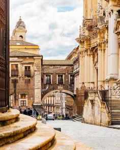 people are walking around in an old european city with stone steps and arches on either side