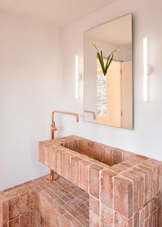 a bathroom sink sitting under a mirror next to a brick counter top with a plant in it