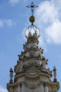 the top of a tall building with statues on it's sides and a weather vane