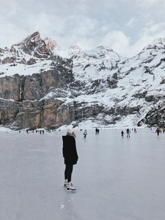 people skating on an ice rink with mountains in the background and snow covered ground around them