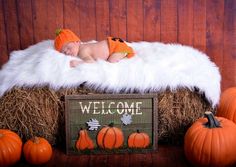 a baby sleeping on top of hay next to pumpkins and a sign that says welcome