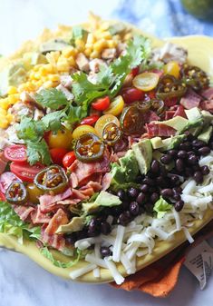 a large salad on a yellow platter with black beans, tomatoes, corn and lettuce