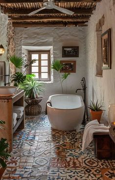 a bath tub sitting next to a window in a bathroom under a ceiling fan and potted plants