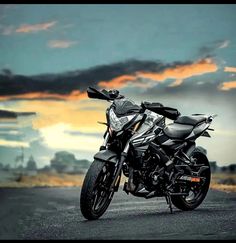 a black motorcycle parked on the side of a road under a cloudy sky with clouds