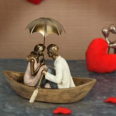 two figurines are sitting in a boat with an umbrella over their heads and one is holding a red heart