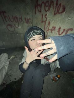 a woman with her hand on her face in front of a graffiti covered wall and wearing a beanie