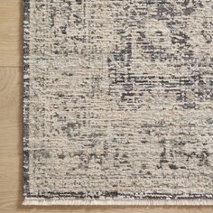 an area rug with grey and white colors on top of a wooden floor in front of a wall