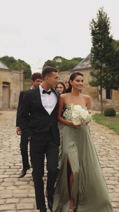 a man in a tuxedo and woman in a dress walking down a cobblestone road