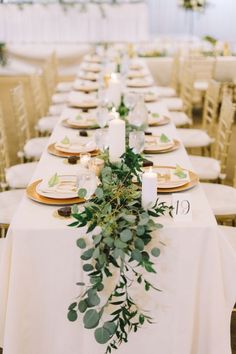 a long table with white linens and greenery is set for an elegant dinner