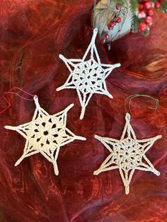 three white crocheted star ornaments sitting on top of a red cloth