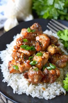 a black plate topped with rice and chicken next to broccoli on a table