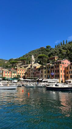 several boats are docked in the water next to some buildings and trees on top of a hill