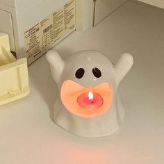 a white candle holder with an orange light in the shape of a ghost