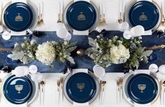 the table is set with blue plates and silverware, white flowers and candlesticks