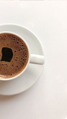 a cup of hot chocolate on a white saucer with a spoon in the middle