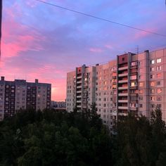 the sky is pink and purple as the sun sets in front of some apartment buildings