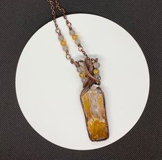 a white plate topped with a necklace and an orange piece of art on it's chain