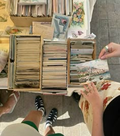 two people sitting at a table with many books and magazines on it, one person is holding an open book