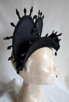 The Queen of Darkness headdress is a glorious Tudor inspired attifet headdress with a gothic twist!This vampire style headdress is covered with black silk shantung and embellished with black cord trimming all around the edges.It is further trimmed with black crystal details that create a halo effect. The piece is completed with a black crystal handmade elements placed at the center of both at the frond as well as the back part,to add that extra drama that we all love! The base is a headband styl Gothic High Crown Costume Accessories For Costume Party, Black Fitted Fantasy Costume Hats And Headpieces, Gothic Fitted High Crown Costume Accessories, Fitted Costume Hat With Tall Crown, Fitted Tall Crown Costume Hats, Gothic Costume Accessories For Theater And Carnival, Black High Crown Halloween Costume Hat, Handmade Gothic Costume Accessories, Black Punk Costume Hats And Headpieces