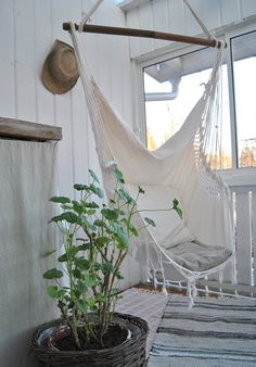 a hammock hanging from the side of a white wall next to a potted plant