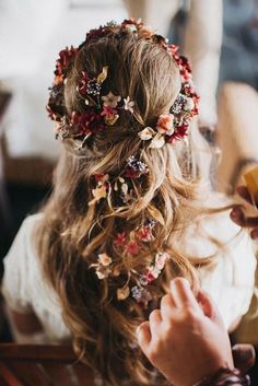 a woman is getting her hair done with flowers in her hair and sitting on a chair