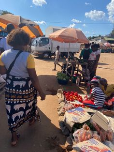 a woman standing next to a table filled with fruit and veggies at an outdoor market