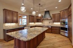 a large kitchen with wooden cabinets and marble counter tops, along with an island in the middle