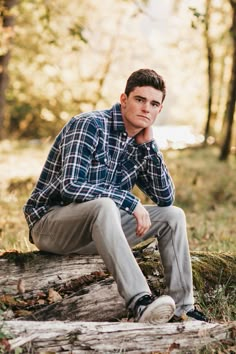 a man is sitting on a log in the woods with his hand under his chin