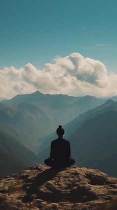 a person sitting on top of a mountain with mountains in the background and clouds in the sky