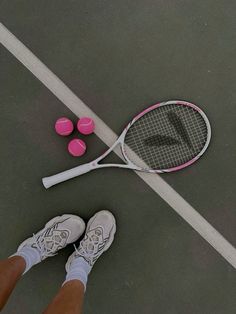 a tennis racquet and three pink balls on the ground next to a woman's feet