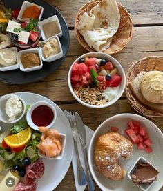 a table topped with plates of food and bowls of fruit next to each other on top of a wooden table