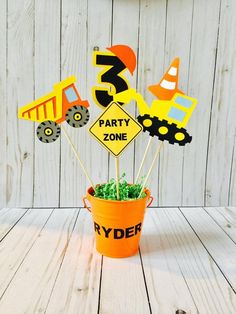 a birthday cake topper sitting in a bucket filled with construction themed cupcakes