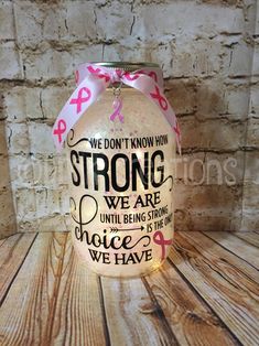 a jar with pink ribbon on it sitting on top of a wooden table next to a brick wall