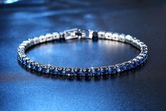 A classic tennis bracelet with a colorful surprise. 28 of the highest quality Sapphire Blue Swiss CZ diamonds in a solitaire pattern. The setting is triple platinum clad (highest quality platinum plating) and each stone is prong-set for security. Snap hook closure for comfort and security. Flexible for comfort--can be worn all day! Swiss CZs are known for their sparkling reflection of light with deep colors. Very versatile can be worn every day or for a special occasion. Coordinates well with yo Blue Brilliant Cut Tennis Bracelet For Gift, Sapphire Cubic Zirconia Tennis Bracelet, Blue Brilliant Cut Tennis Bracelet Gift, Blue Tennis Bracelet With Prong Setting For Formal Occasions, Blue Cubic Zirconia Bracelets For Party, Blue Cubic Zirconia Bracelet For Party, Blue Cubic Zirconia Tennis Bracelet With Brilliant Cut, Silver Sapphire Tennis Bracelet With Brilliant Cut, Blue Tennis Bracelet With Prong Setting