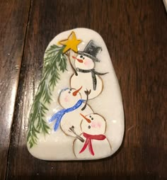 three snowmen with hats and scarfs are painted on a white marble rock, sitting on a wooden table