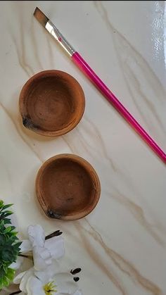 two wooden bowls and a pink brush on a white surface with flowers in the foreground