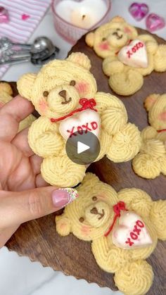 a person holding a teddy bear cookie in front of some cookies on a wooden platter