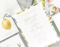 the wedding stationery is laid out on top of each other, with oranges and leaves