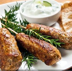 some meat skewers are sitting on a plate with dips and bread sticks