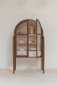 a wooden cabinet with glass doors and drawers on the bottom shelf, in front of a white wall