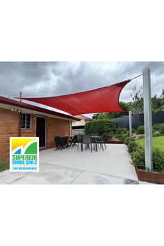 an outdoor patio area with a red shade sail over the dining room table and chairs