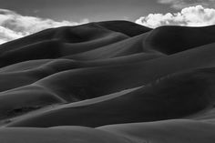 black and white photograph of sand dunes with clouds in the background