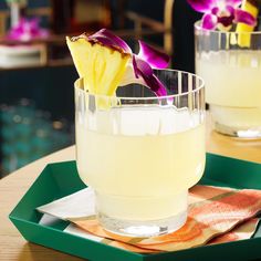 two glasses filled with drinks sitting on top of a green tray next to each other