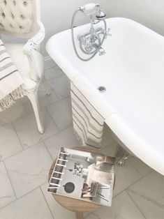 a white bath tub sitting next to a magazine on top of a wooden table in a bathroom