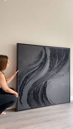 a woman kneeling down next to a large black painting on the wall in an empty room