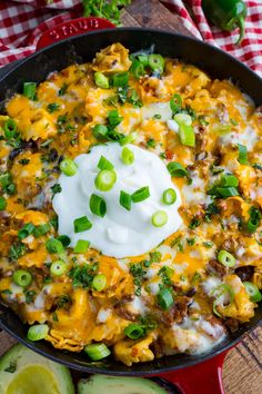 a skillet full of mexican food with sour cream and green onions on the side